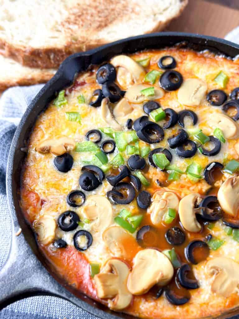 A pan of delicious pizza topped with black olives, green peppers and  mushrooms, and soaked with yummy sauce. 