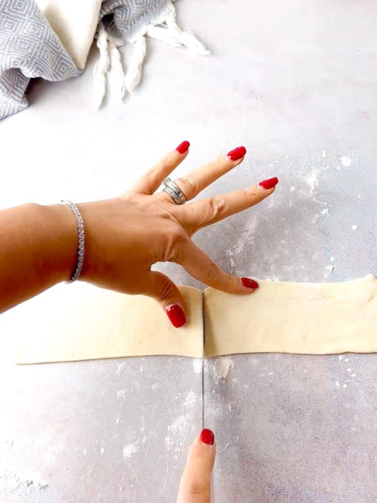a woman cutting puff pastry rectangle into two equal parts