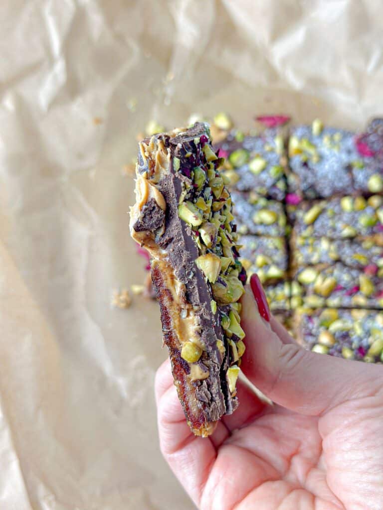 A mouth watering date bark creation adorned with finely diced peanuts, pistachios, grated coconut, and a scattering of dried rose petals