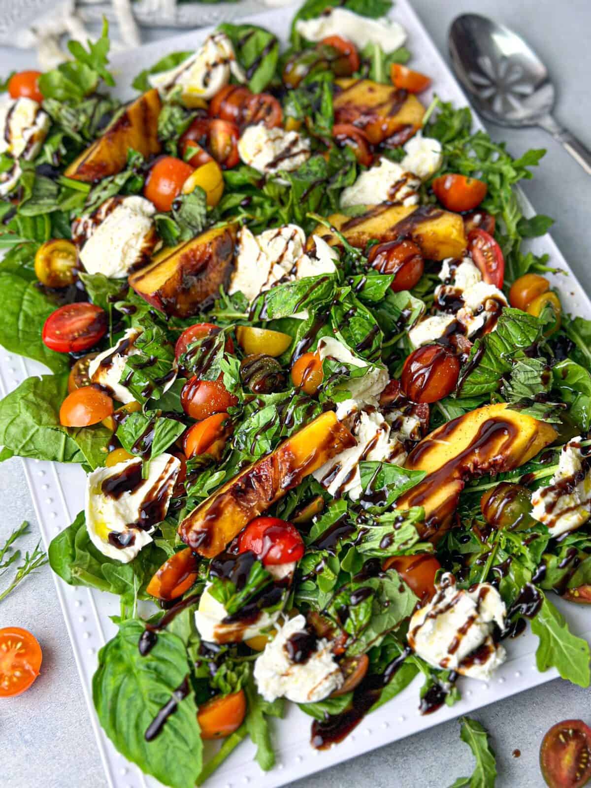 a dish of peach and arugula salad with burrata cheese and cherry tomatoes and drizzled with balsamic vinaigrette
