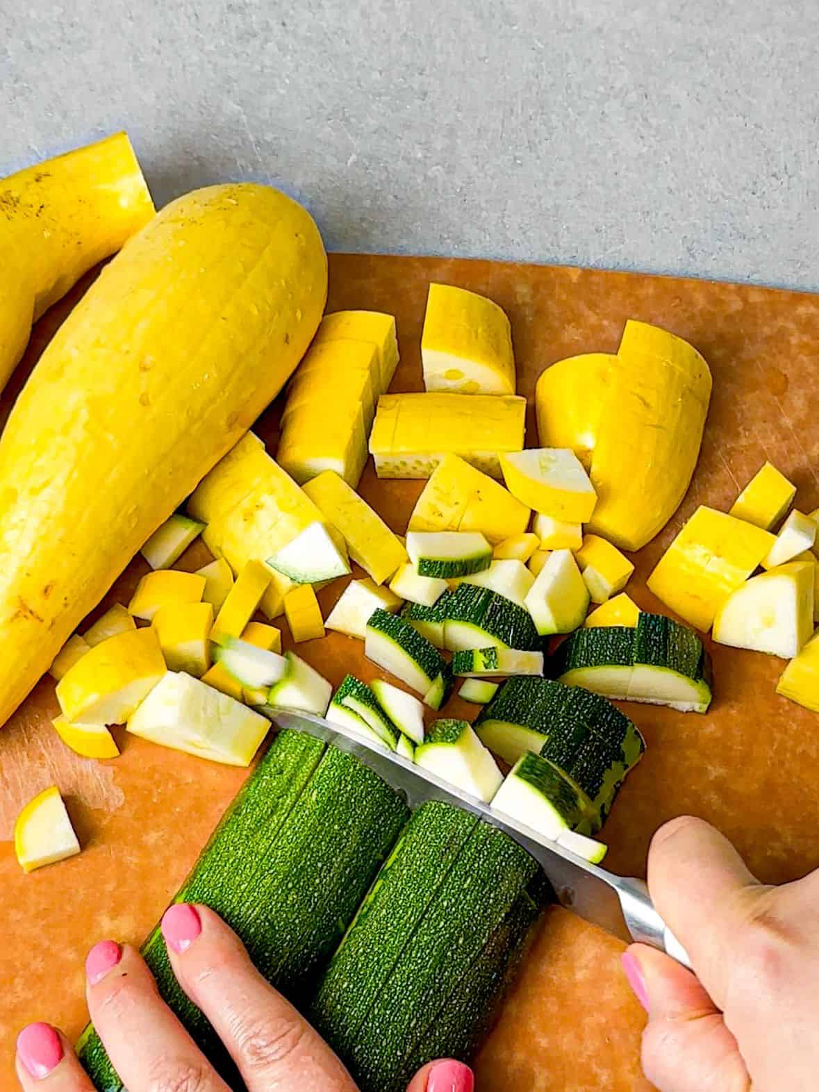 a woman cutting yellow and green squash into small cubes
