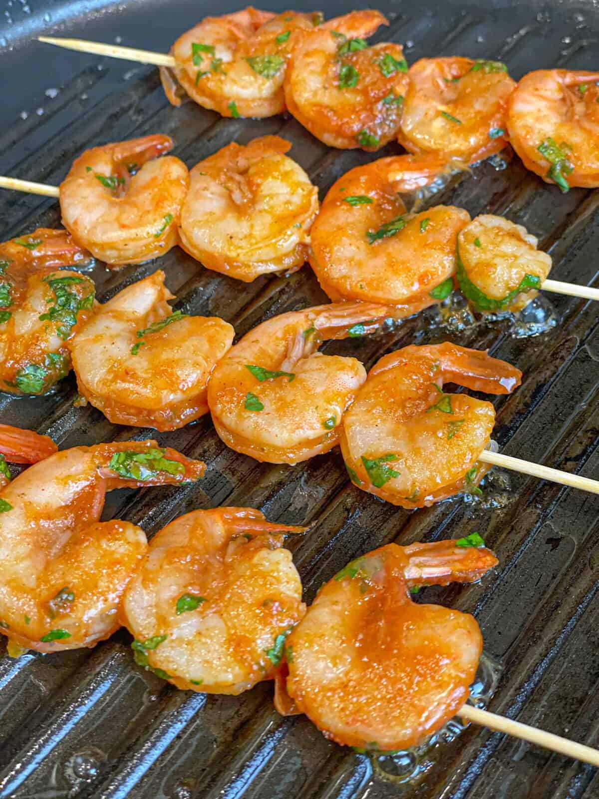 raw marinated shrimp on skewers stacked on a white glass plate