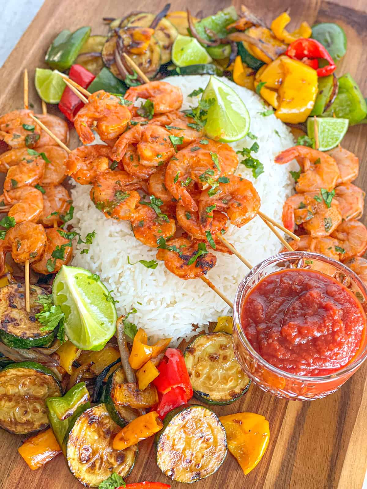 grilled cilantro lime shrimp on top of a bed of white rice surrounded with grilled veggies and seafood cocktail sauce