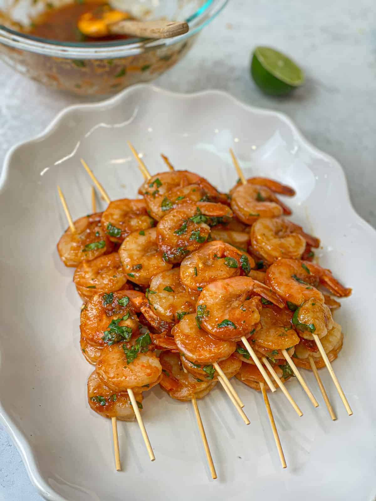 raw marinated shrimp on skewers stacked on a white glass plate