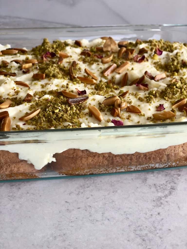 Delicious Aish El Saraya dessert, featuring layers of soft bread soaked in sweet syrup, topped with a creamy custard, garnished with crushed pistachios and drizzled with rose water syrup.