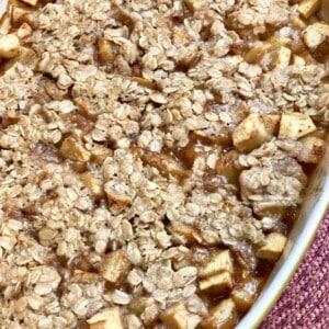 Classic apple crisp in a white pan topped with oatmeal and seasoned with cinnamon and nutmeg