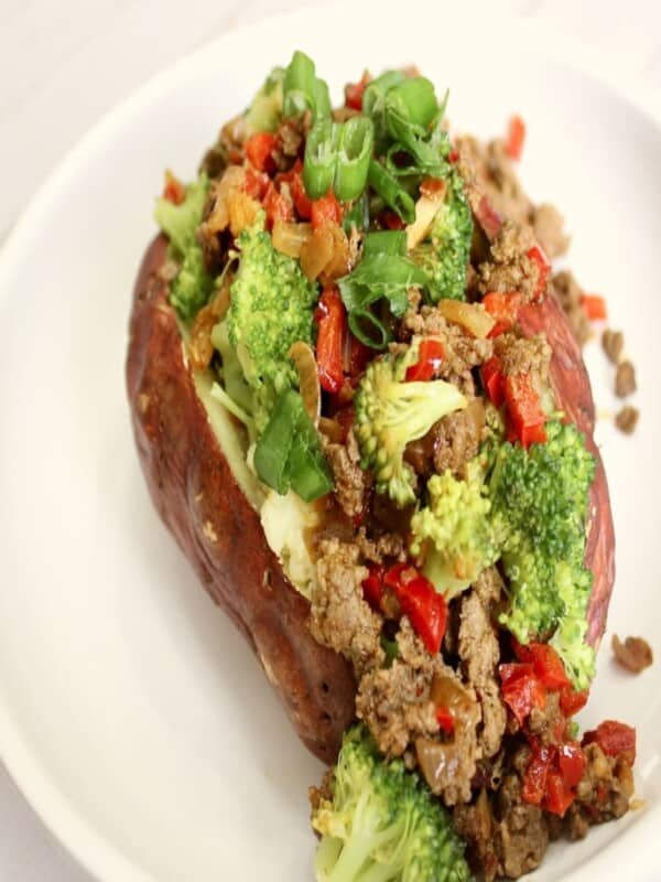 A medium sweet potato with broccoli and beef with garlic, onion, and red bell pepper and s seasoned with chili powder, ground cumin, and salt in a white plate
