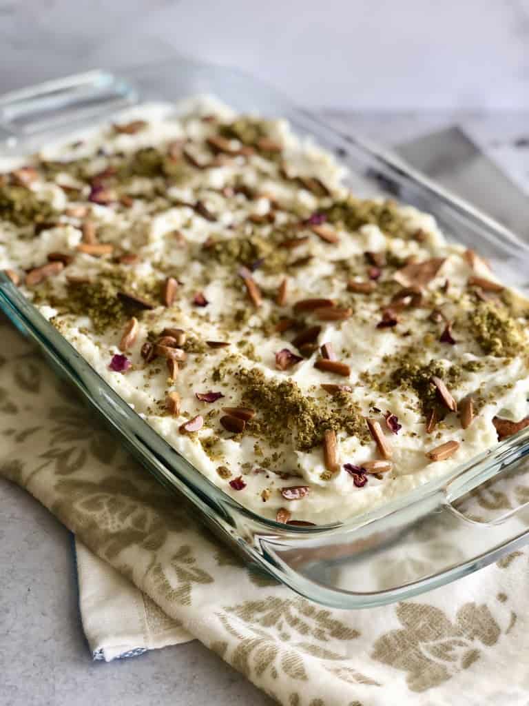 A pan of Aish El Saraya Rose Water Bread Pudding topped with slivered almonds and garnished with ground pistachios