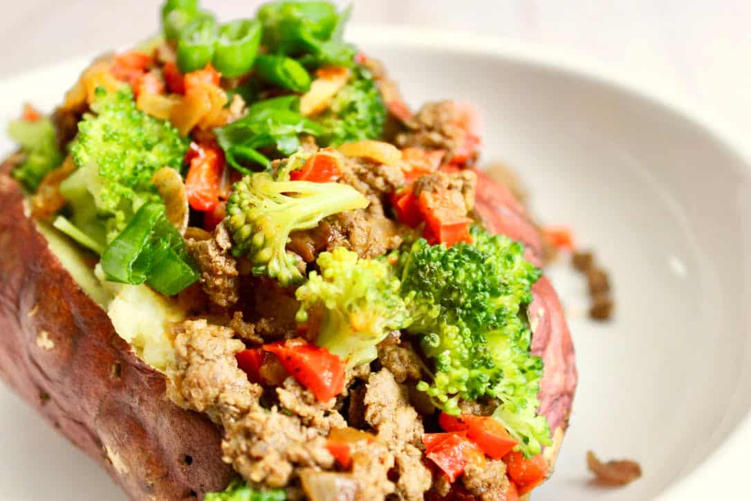 A white plate serving a medium sweet potato with broccoli florets and beef with garlic, onion, and red bell pepper and s seasoned with chili powder, ground cumin, and salt