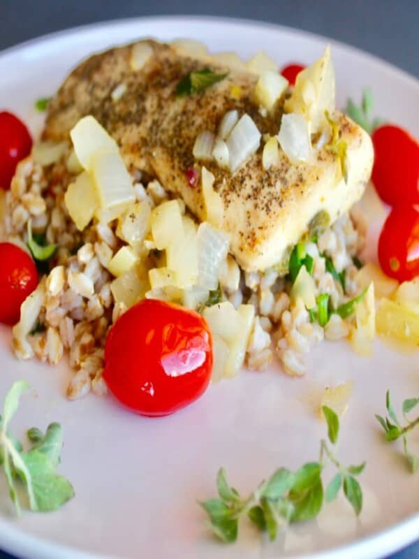 A plate of Mahi Mahi fillet fish with Farro decorated with cherry tomatoes and organo leaves