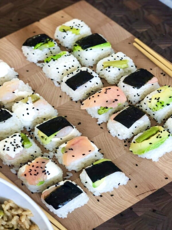 No-roll sushi cubes made with short grain rice, avocado slices, asparagus, cooked shrimp, sushi nori, smoked salmon and decorated with Nigella seeds on a wooden plate