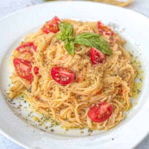 A plate of Tomato Parmesan Spaghetti garnished with basil and a sprinkle of parmesan