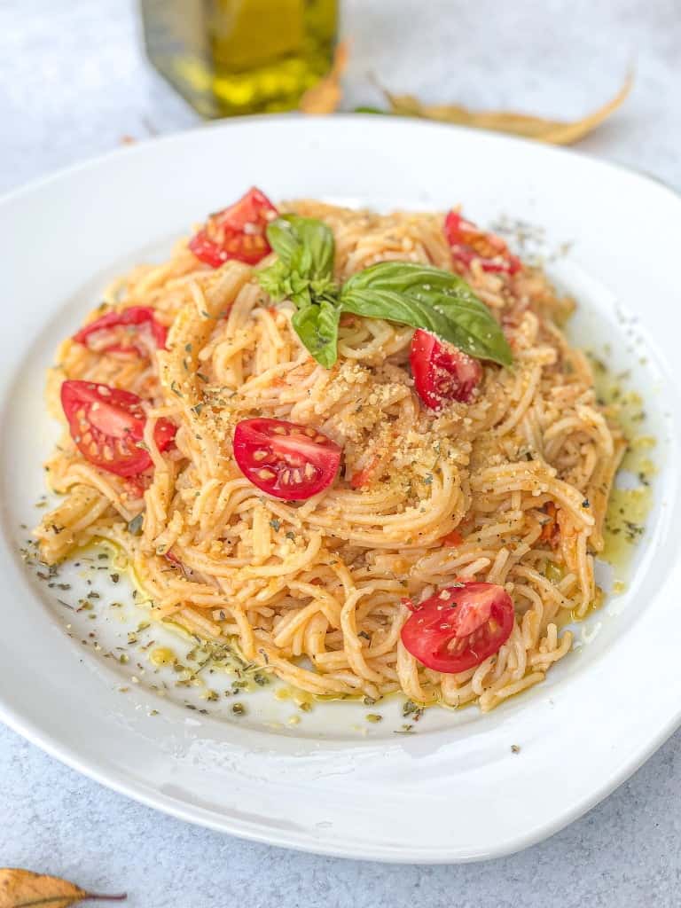 A plate of Tomato Parmesan Spaghetti garnished with basil and a sprinkle of parmesan