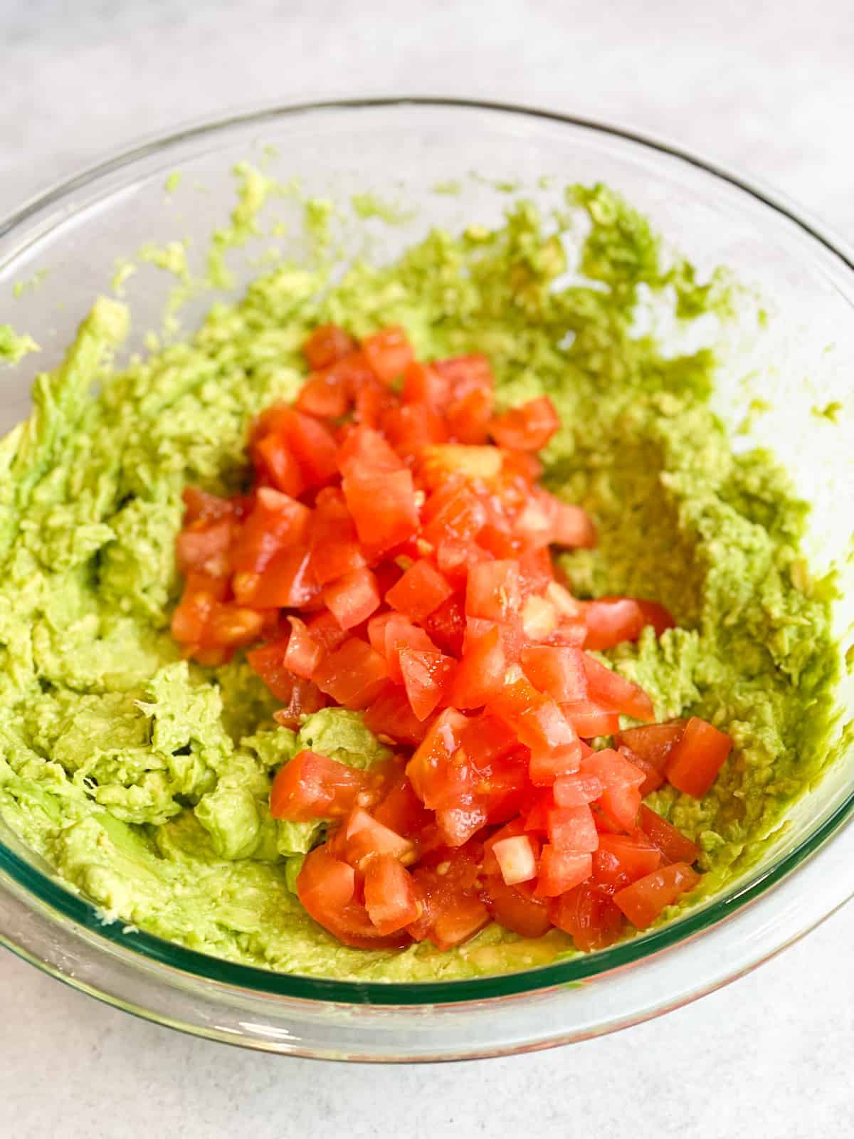 A bowl of mashed avocadoes with squared slices of tomatoes.