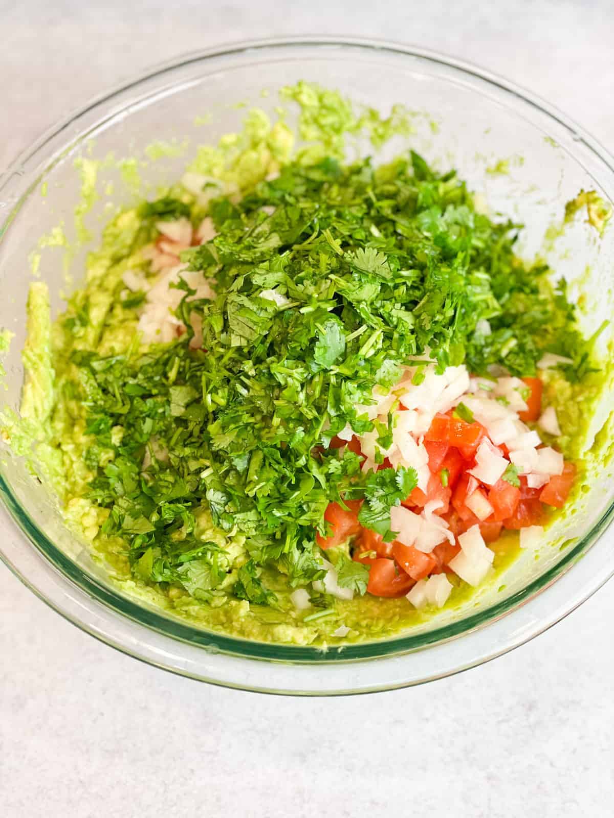 A bowl full of mashed avocadoes, slices of tomatoes and onions, and parsley.
