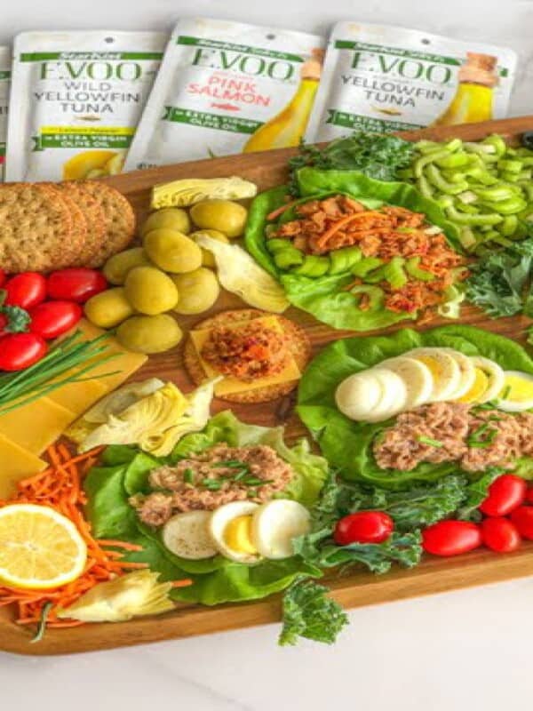 a lunch board with tuna, fresh veggies, Kalamata olives, crackers, eggs, and seasonings