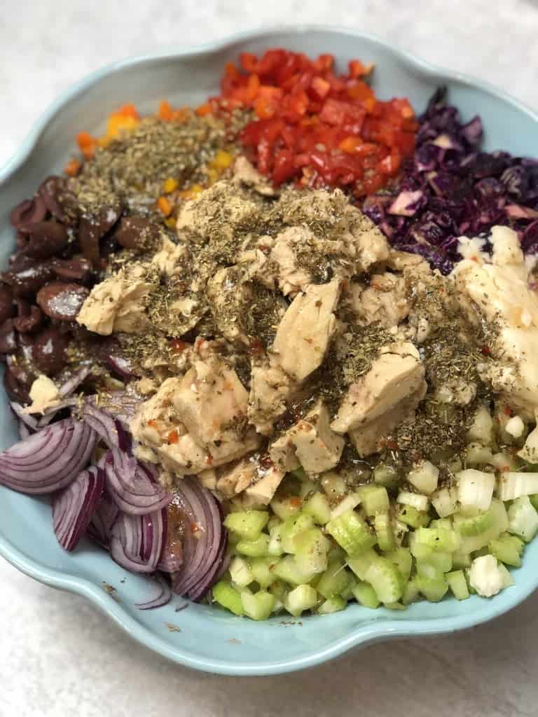 A bowl of chopped veggies like peppers, celery, Kalamata olives, onions, and Tuna topped with seasonings to make Italian Seasoned Tuna Pasta Salad