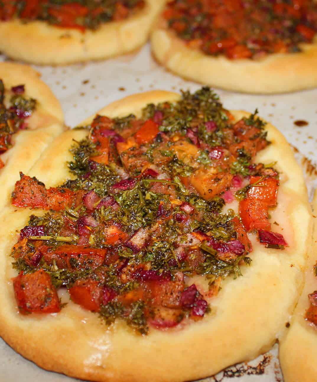Mini Homemade Veggie Pizza topped with a mix of tomatoes, onions, sumac, olive oil, dried mints, and parsley.