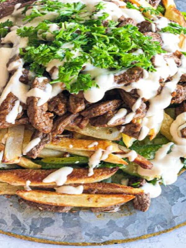 Well seasoned shawarma on top of a layer of greens an baked potatoes and topped with tahini sauce and a sprinkle of chopped parsley