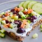 a plate with loaded toast with labneh spread topped with finely chopped Kalamata olives, cucumbers, and tomatoes