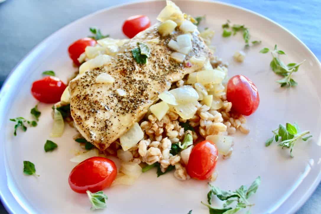 a plate of Mahi Mahi with Farro decorated with cherry tomatoes, onions, and oregano leaves