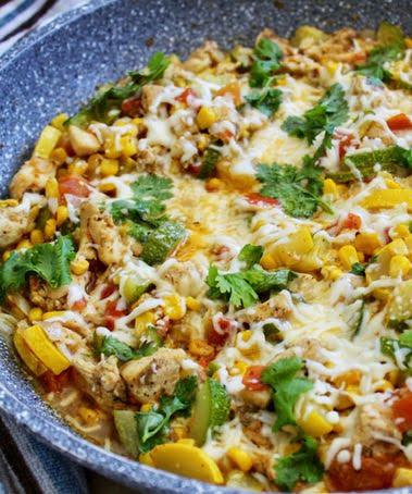 A skillet of tender chicken breasts and chicken thighs with taco seasonings and avocado, corn, black beans, onions, and cilantro topped with mozzarella cheese