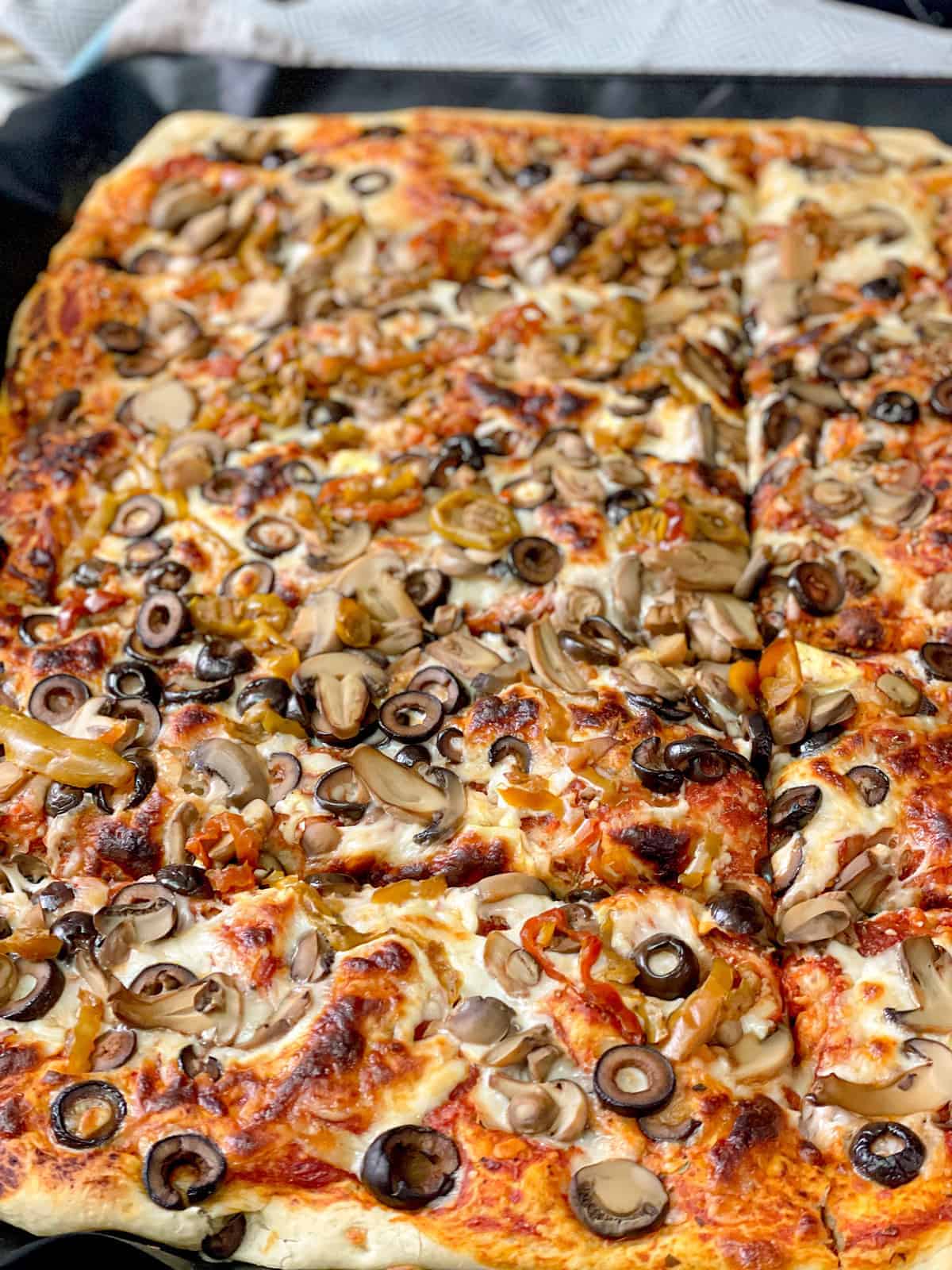 A baked pizza dough topped with melted mozzarella cheese, black olives, mushrooms, pasta sauce and oregano. 