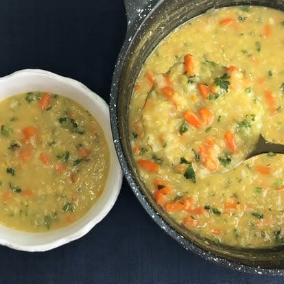 A pot of red lentil soup with chopped carrots, parsley, and onions