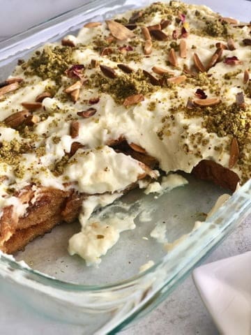 An exquisite serving of Aish El Saraya, a traditional Lebanese dessert. Layers of soft bread soaked in sweet syrup and topped with a creamy custard, garnished with crushed pistachios and drizzled with rose water. A delightful treat with a rich history and delightful flavors
