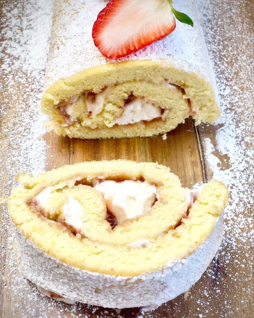 Strawberry Cheesecake Roll stuffed with strawberry jam and cream with a sprinkle of powdered sugar and a slice of strawberry