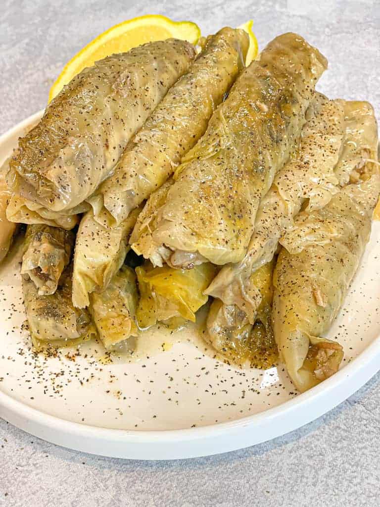 cooked rolled or stuffed cabbage (malfoof) in a white plate decorated with dried mint leaves and lemon wedges