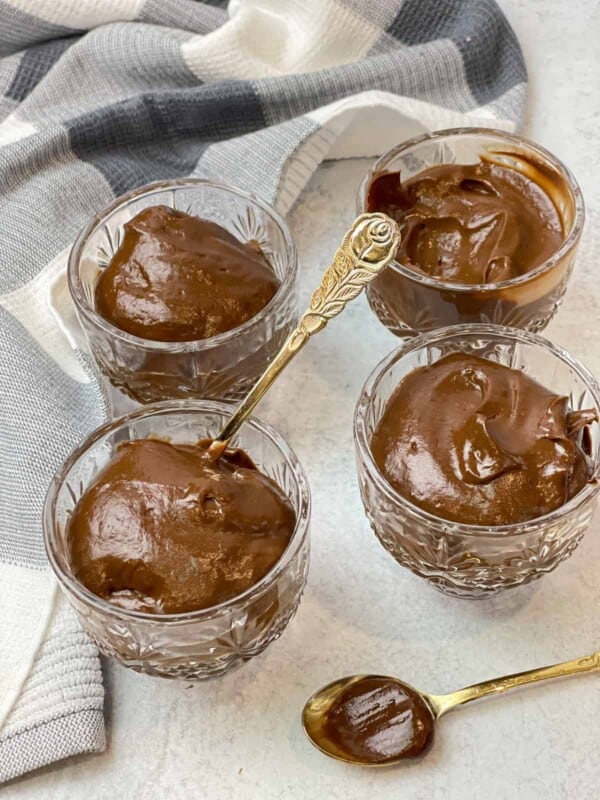 Four cups of chocolate coffee avocado pudding with a golden spoon placed in one of the cups, and another placed in front of them.