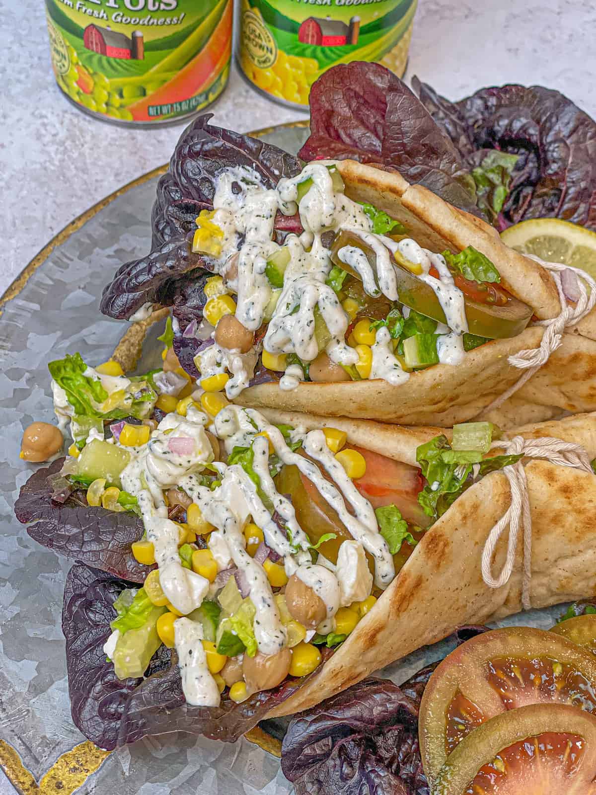 Two pitas stuffed with Mediterranean salad and tied in a beautiful knot. The sandwiches show the ingredients of the salad which are chopped cucumbers, corn, chickpeas, lettuce, and tomatoes, all drizzled with a delicious Mediterranean dressing.