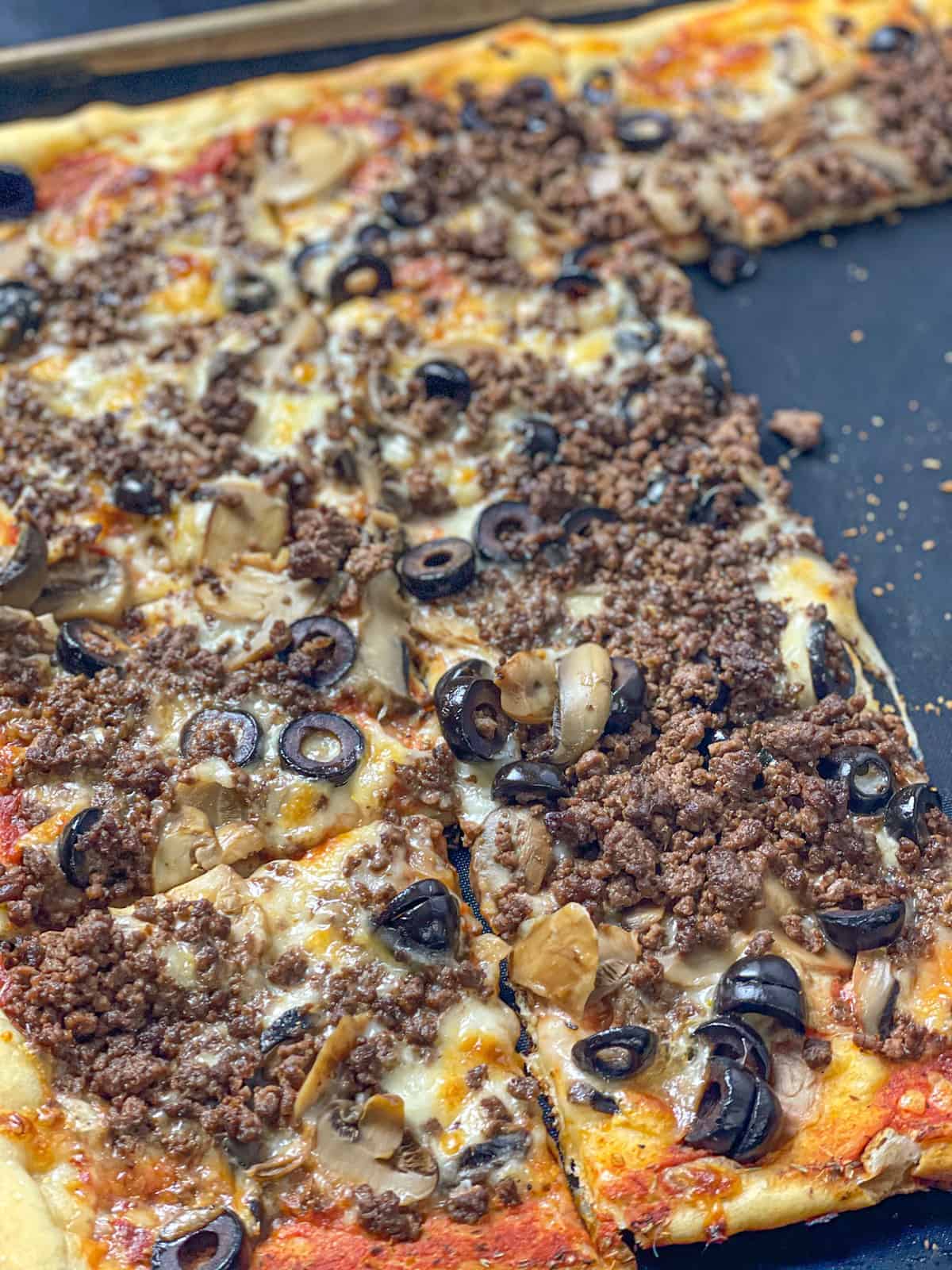 square slices of spicy beef sujuk pizza with olives and mushrooms