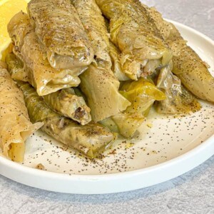 cooked rolled or stuffed cabbage (malfoof) in a white plate decorated with dried mint leaves and lemon wedges