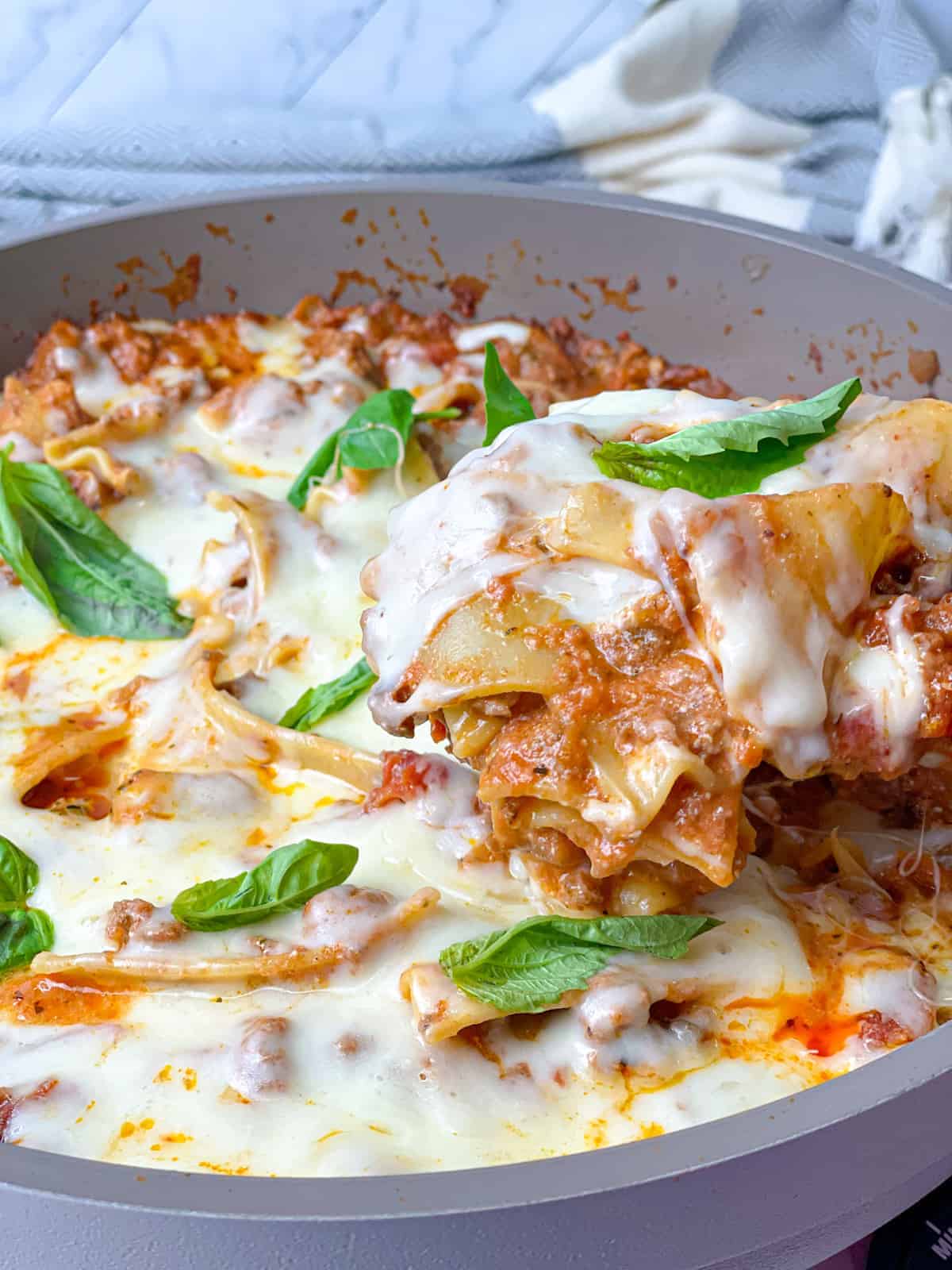 A spoon pulling some juicy lasagna pasta with red sauce, mozzarella cheese, and fresh basil.