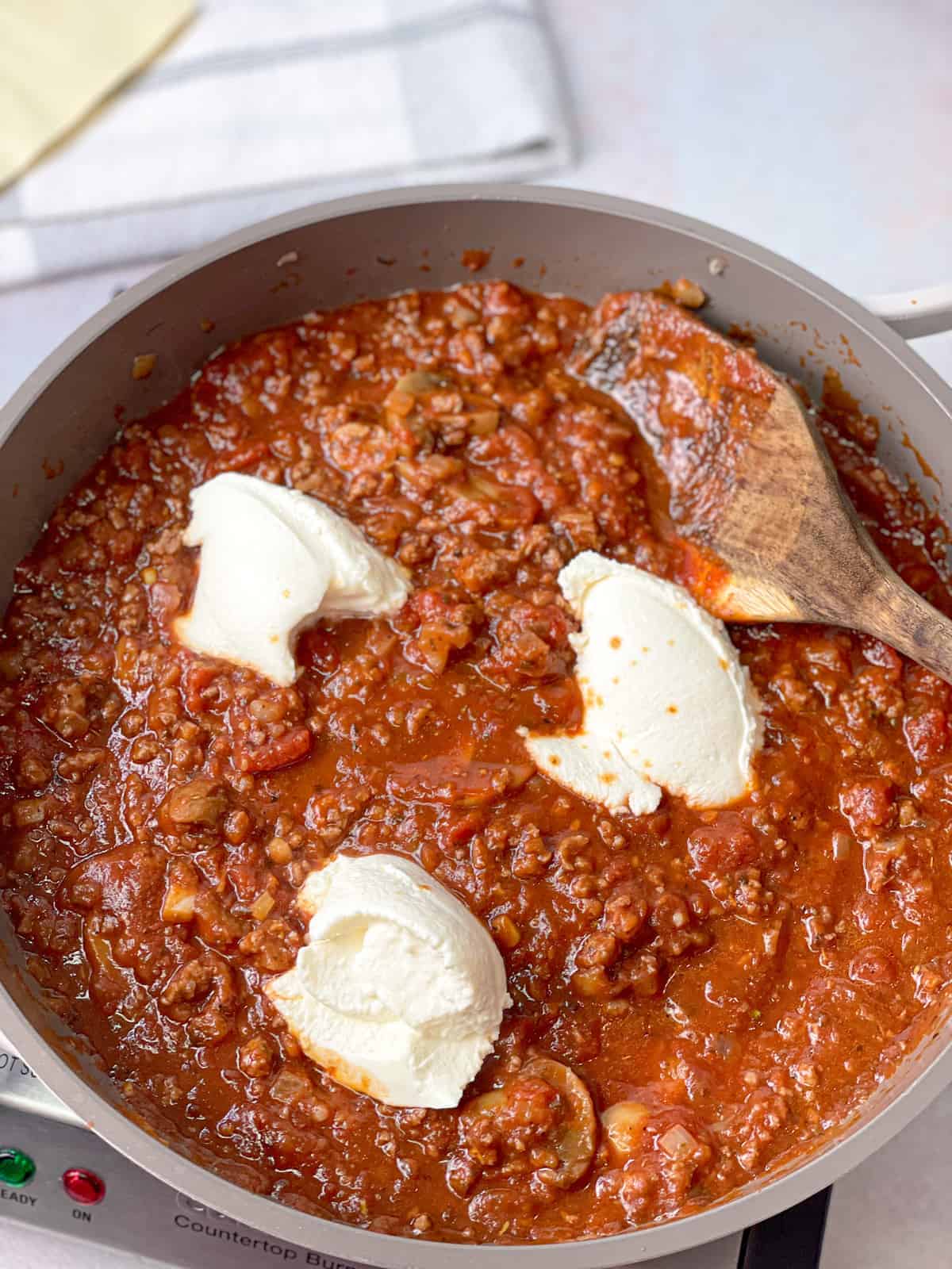 A cooking pan filled with red sauce, minced meat, and ricotta cheese