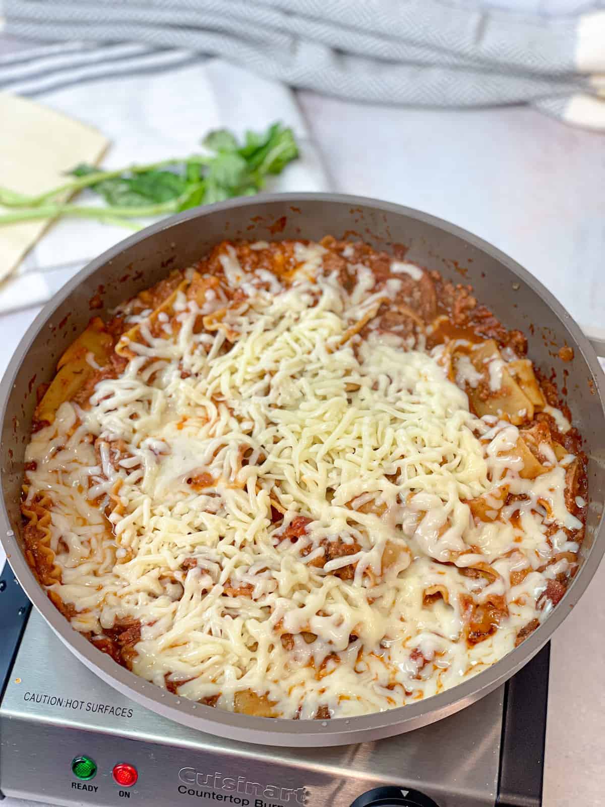 Mozzarella cheese is added to a cooking pan filled with red sauce and lasagna pasta.