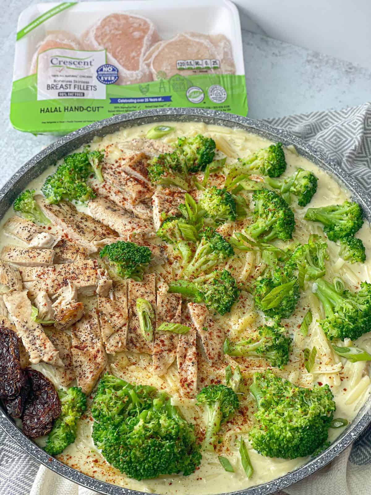 a pan of a pan of Chicken Fettuccine Alfredo made with butter, chicken breast, fettuccine noodles, and broccoli florets topped with grated parmesan