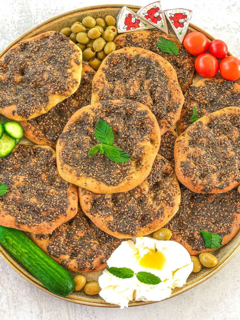 An attractive picture of Zaatar Manakeesh on a tray with a side of labne, tomatos and cucumbers.