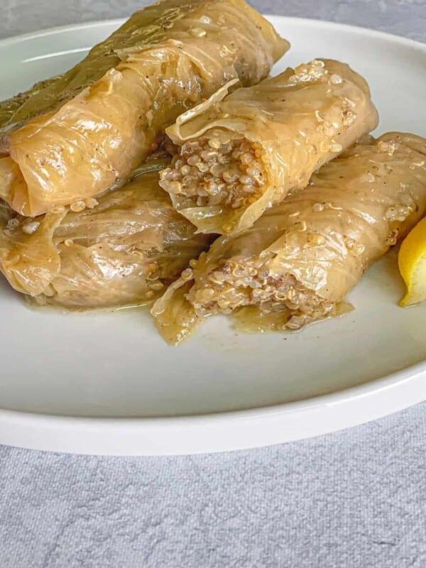 5 quinoa stuffed cabbage rolls on a white plate with lemon wedges