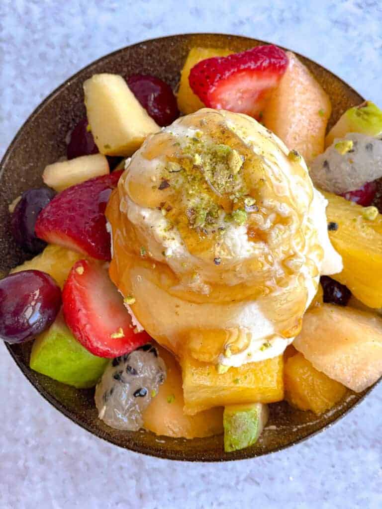 "Fruit salad with ashta: Fresh strawberries, grapes, and pineapple combined with creamy ashta (Lebanese clotted cream), adorned with pistachios and drizzled with honey for a delightful dessert.