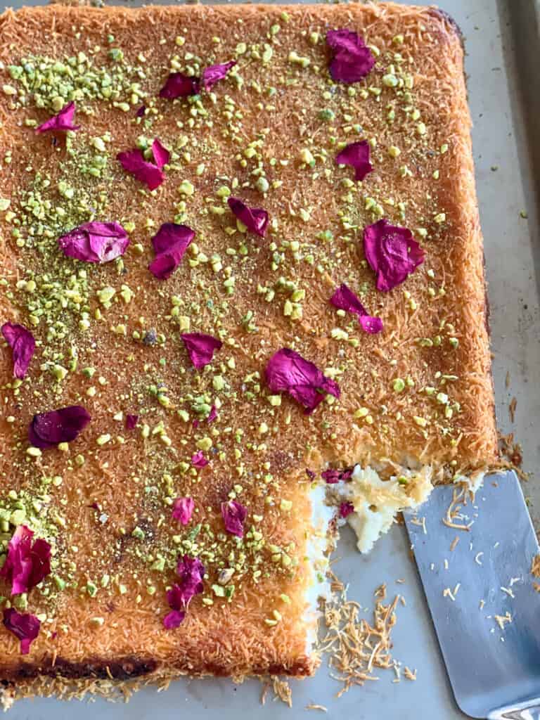A traditional Middle Eastern dessert made of shredded phyllo dough layered with sweet cheese, soaked in syrup, and garnished with pistachios