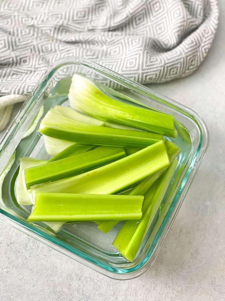 fresh celery stalks stored in water in a glass container