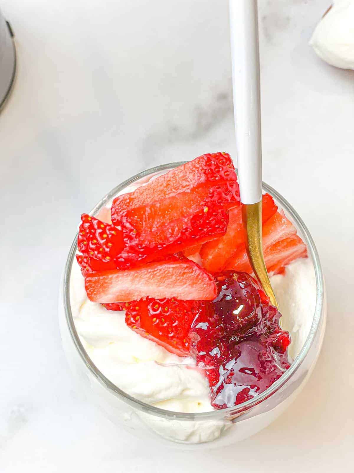A glass of whipped creamed topped with strawberries and sauce.