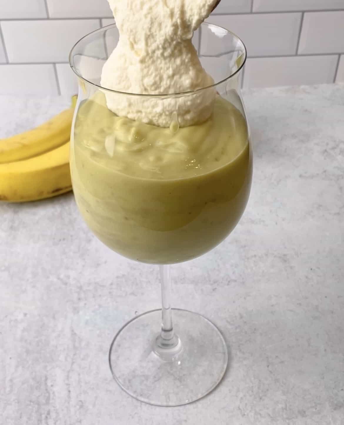 Mashed avocados with honey and milk are placed in a glass with some whipped cheese is drizzled over them.