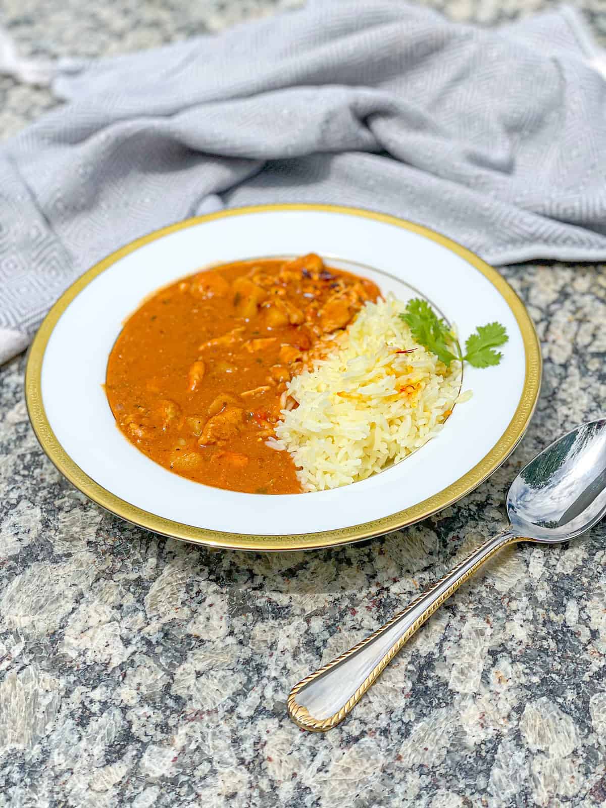 a plate of chicken tikka masala made by combining cubed chicken, potatoes, and onions infused with spices like curry, coriander, and cumin in a creamy tikka masala simmered sauce