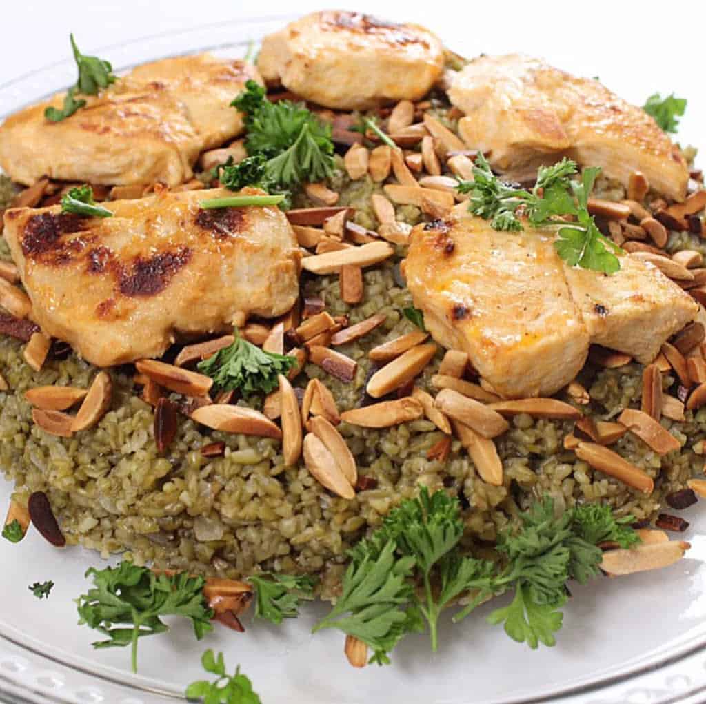 A plate of freekeh topped with golden ginger chicken, fresh parsley, and crunchy nuts.