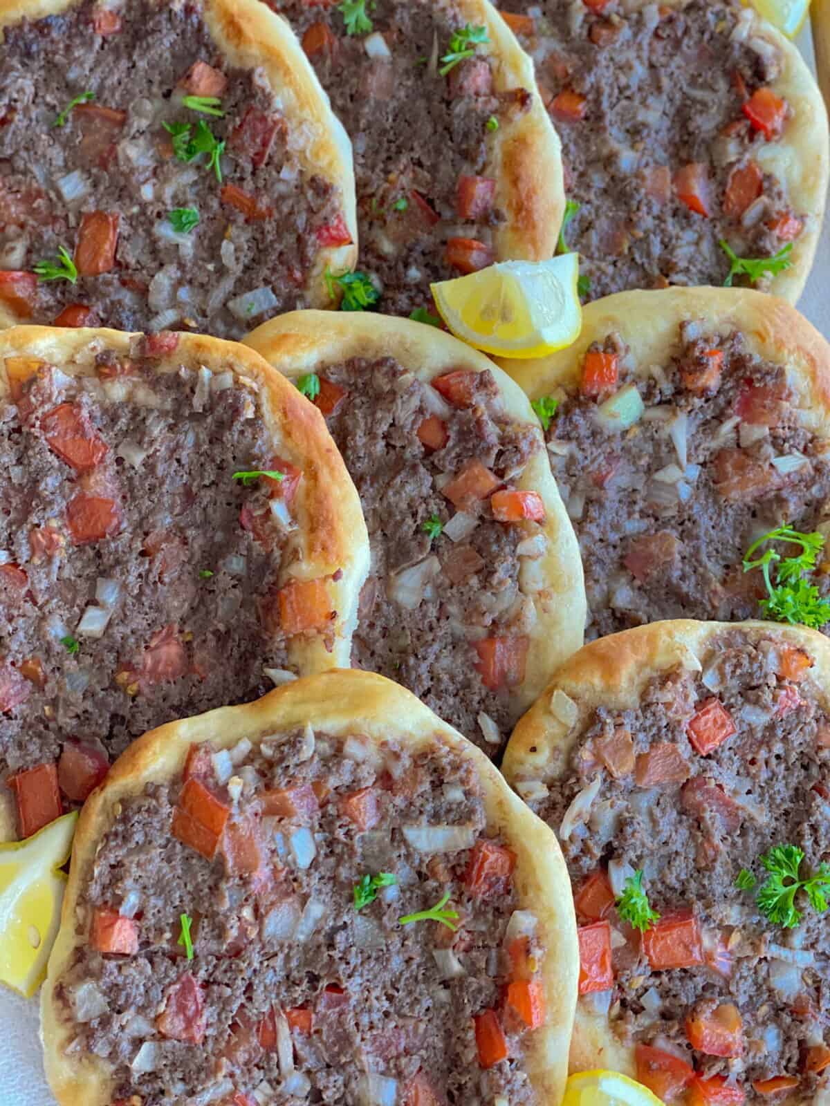 pieces of Lebanese meat pie served on a white plate alongside lemon wedges sprinkled with finely chopped parsley