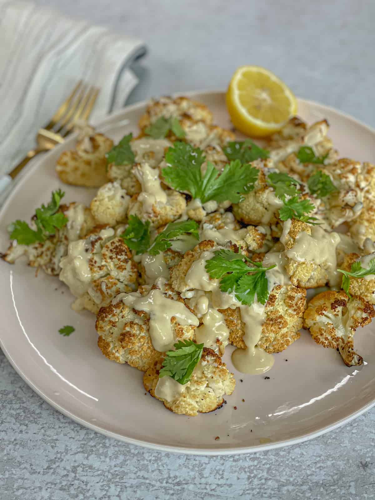 A plate of roasted cauliflower with a side of lemon and a tahini dressing topping.